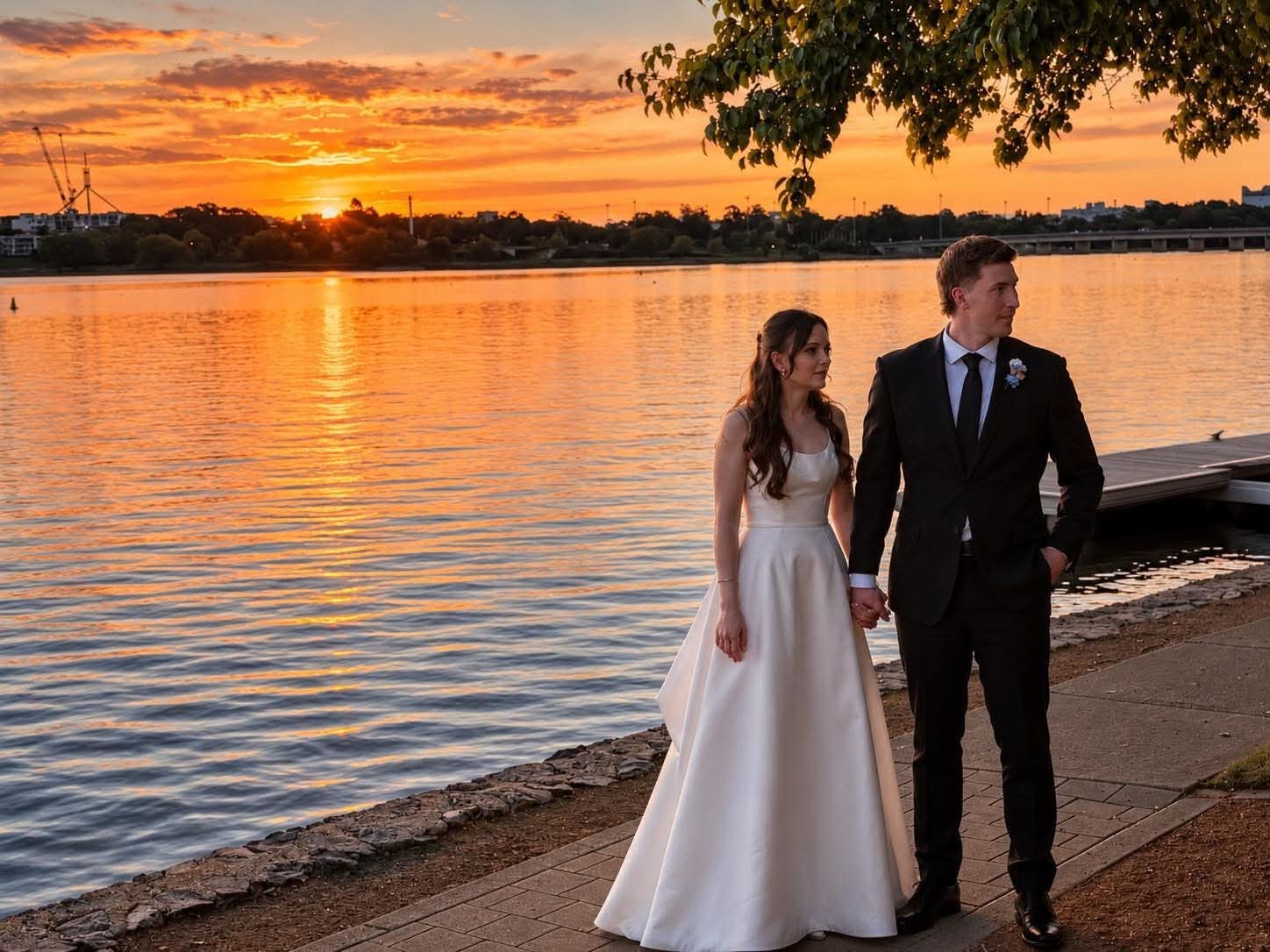 A bride and groom holding hands on a lakeside path at sunset, Canberra.